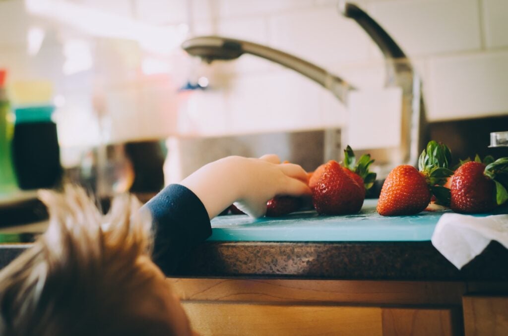 Main d’un jeune enfant attrapant des fraises fraîches sur un plan de travail, activité de découverte alimentaire