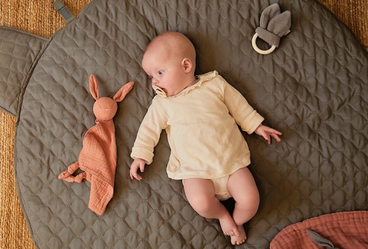 Bébé allongé sur un tapis d’éveil matelassé avec un doudou lapin, activité sensorielle inspirée de la méthode Montessori