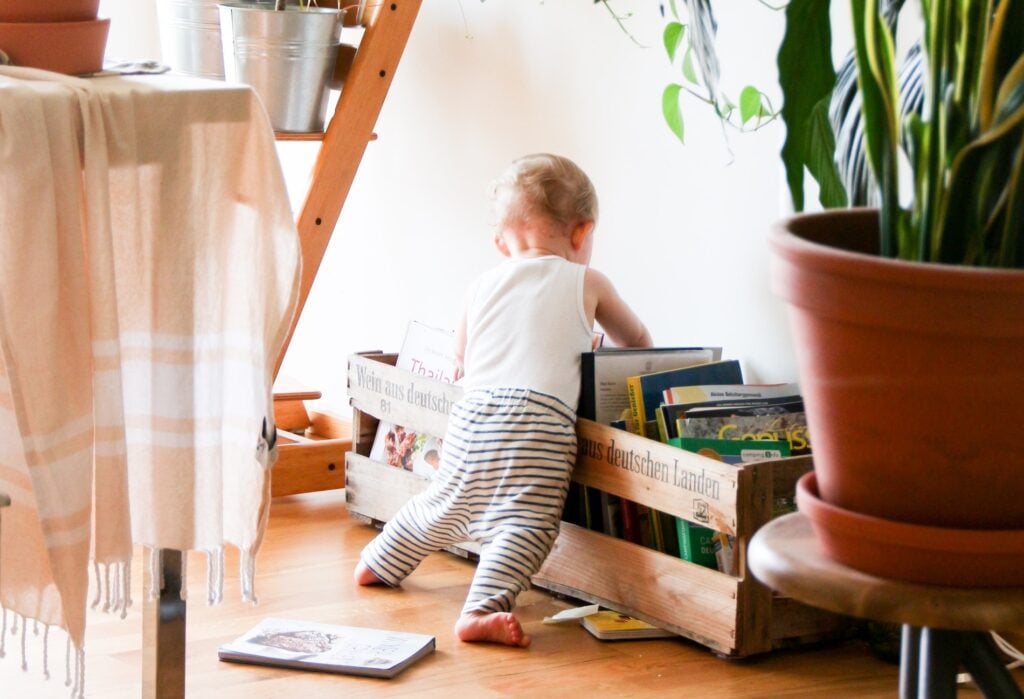 Bébé en pyjama rayé explorant une caisse en bois remplie de livres, éveil à la lecture et autonomie