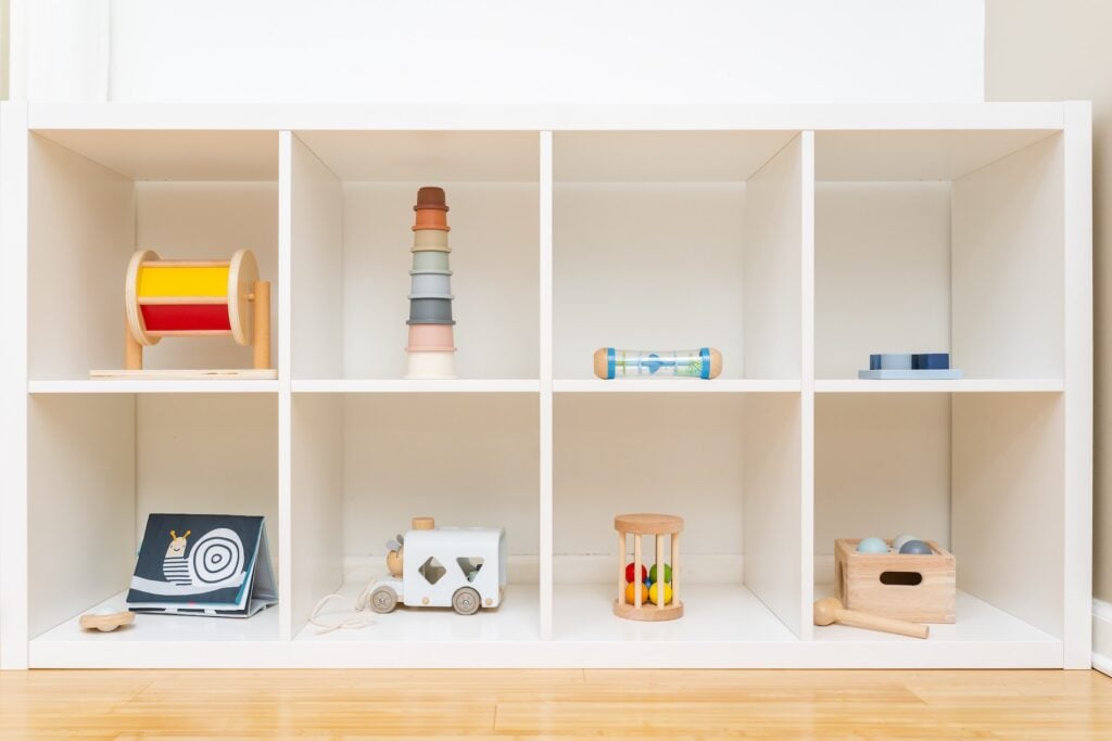 Étagère blanche avec jouets en bois et jeux sensoriels Montessori rangés par catégorie, aménagement minimaliste pour enfant