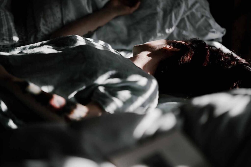 Future maman allongée dans un lit, baignée de lumière douce, se reposant pour préserver son énergie avant l’accouchement.