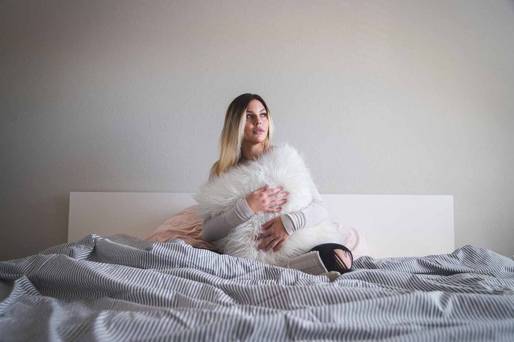 Future maman assise dans son lit, tenant un coussin moelleux, profitant d’un moment de repos pendant la grossesse.