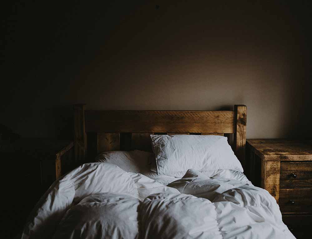 Lit en bois avec oreillers et couette défaits, symbole de sommeil réparateur essentiel pendant la grossesse.