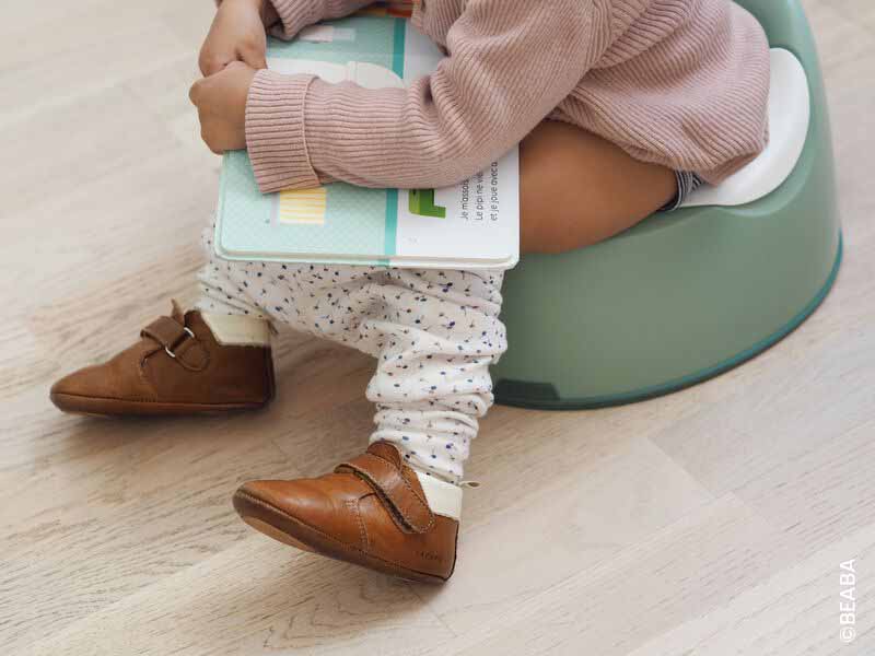 Bébé assis sur un pot avec un livre, réussite de la propreté pour les tout-petits.
