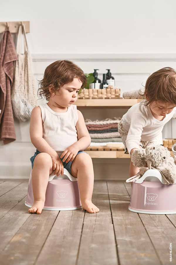Deux jeunes enfants assis sur des pots pour bébé dans une salle de bain moderne. Âge idéal pour commencer le pot pour bébé pour les parents qui se questionnent sur quand mettre bébé au pot