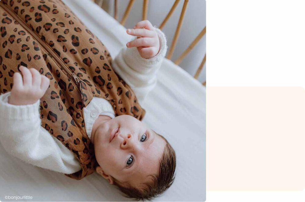 Bébé allongé sur le dos dans une gigoteuse à imprimé léopard, concentré sur son environnement pendant une activité bébé 4 mois sur le tapis d’éveil