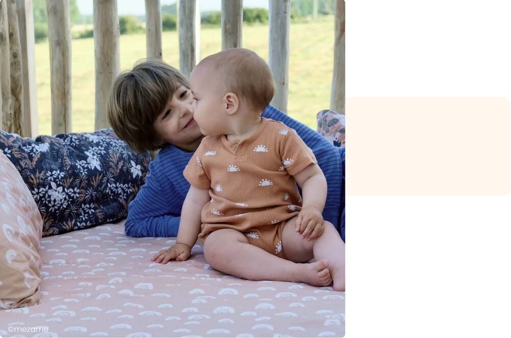 Bébé et grand frère allongés sur un matelas à l’extérieur, moment complice activité bébé 10-12 mois