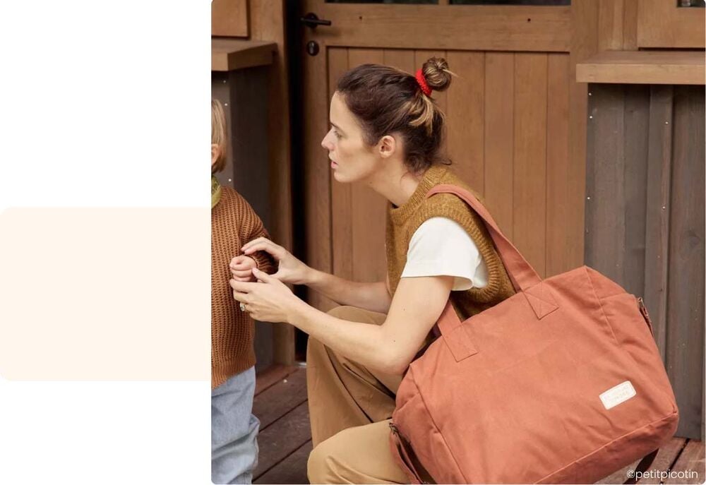 Période d’adaptation crèche bébé, parent accroupi devant son bébé pour l’aider à se préparer avant la journée à la crèche