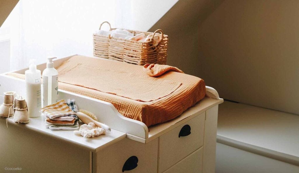 Coin à langer en bois clair recouvert d’un lange terracotta, accompagné d’accessoires pour le change du bébé