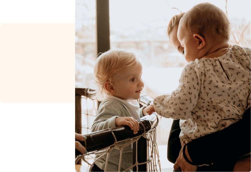 Premier jour crèche bébé, deux enfants se rencontrant et échangeant un sourire sous le regard d’un adulte