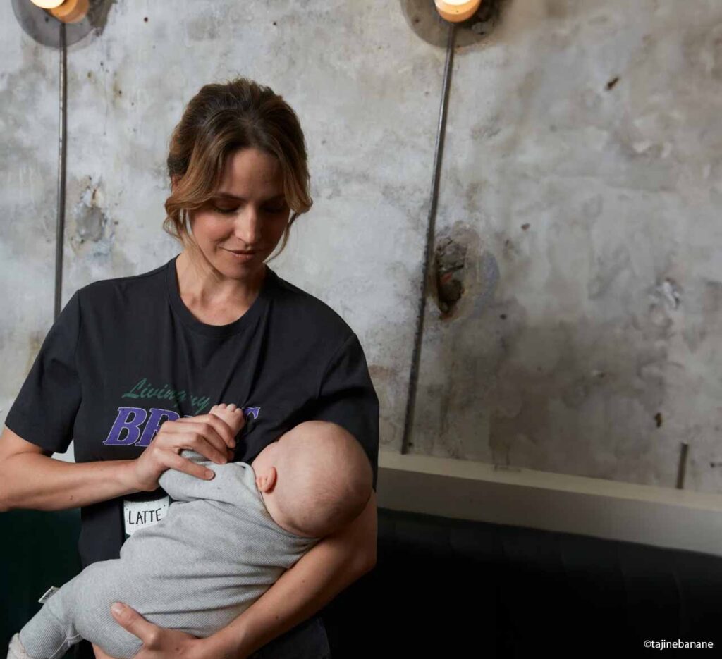 Femme en t-shirt noir utilisant une écharpe de portage pour allaiter son bébé confortablement, technique pratique pour allaiter en public