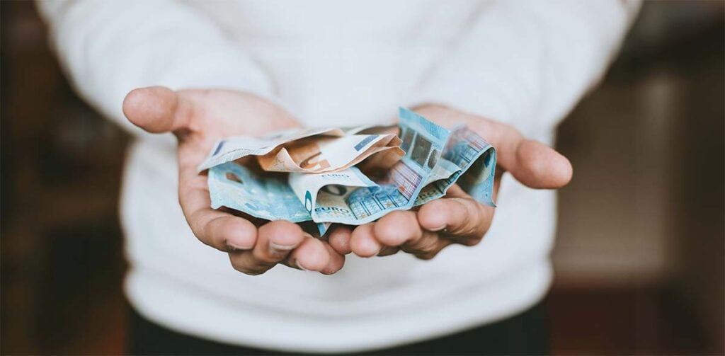 Billets d’euros présentés dans les mains, symbolisant les aides financières adoption enfant et le soutien économique disponible pour les futurs parents