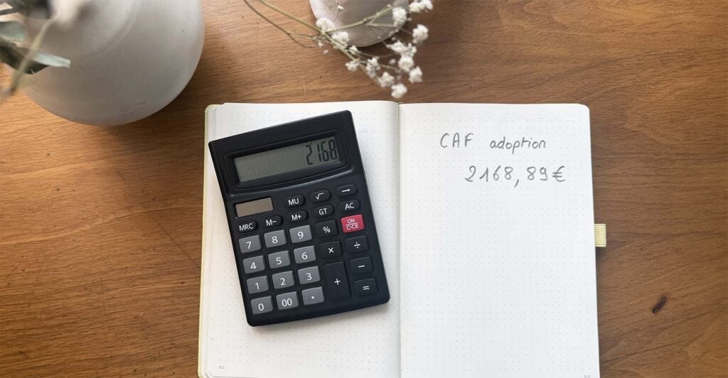 Carnet indiquant le montant d’une aide CAF avec calculatrice, illustrant le calcul des aides financières adoption enfant