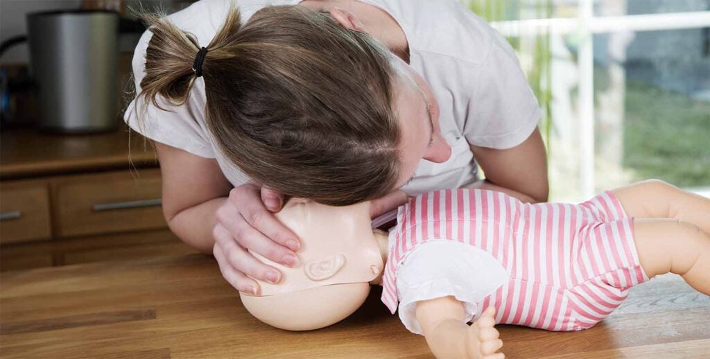 Parent réalisant les gestes premiers secours bébé en cas d’arrêt respiratoire sur mannequin pour savoir réagir rapidement en situation d’urgence