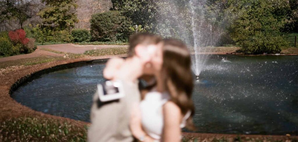 Couple enlacé dans un parc avec fontaine célébrant l'annonce de la grossesse et l'implication du partenaire