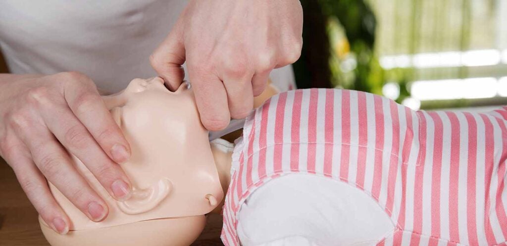 Parent apprenant les gestes premiers secours bébé en cas d’étouffement, avec positionnement précis des mains pour dégager les voies respiratoires d'un nourrisson en urgence