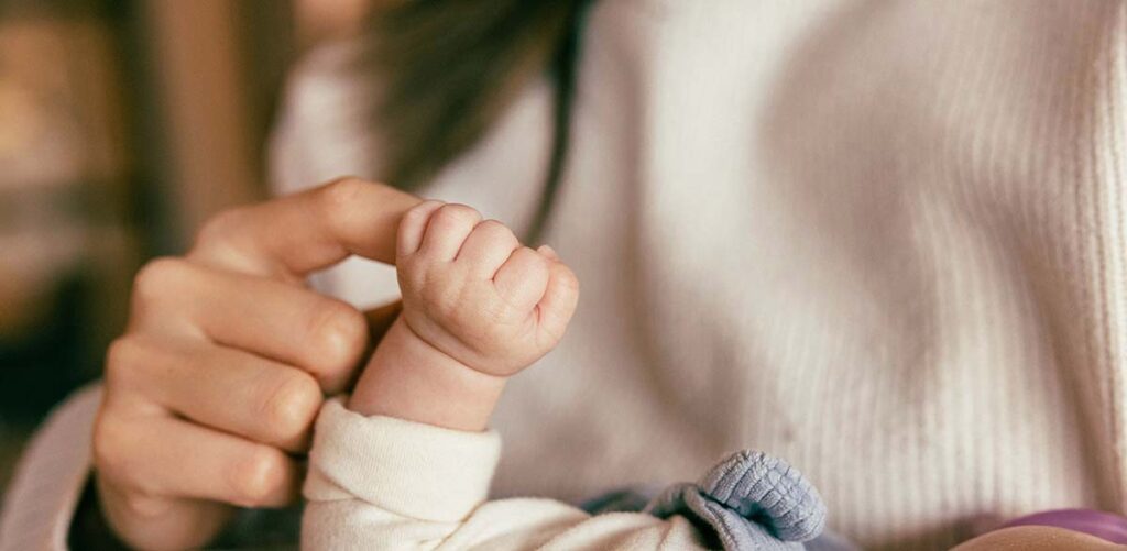 Main d’un parent tenant le poing d’un nouveau-né, illustrant le congé maternité après la naissance