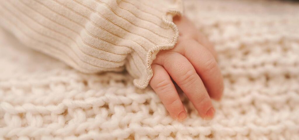 Gros plan sur la main d’un bébé posé sur une couverture, évoquant le congé maternité en France