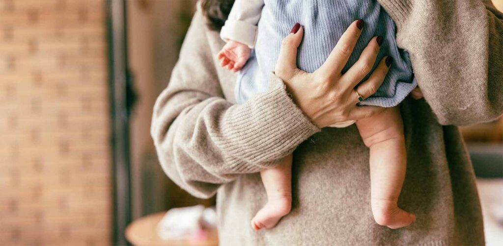 Parent portant un nourrisson contre lui, illustrant les informations essentielles sur le congé maternité