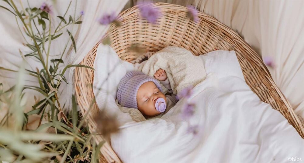 Bébé endormi dans un couffin en osier, inspiration liste naissance printemps avec essentiels nouveau‑né mi‑saison et linge léger