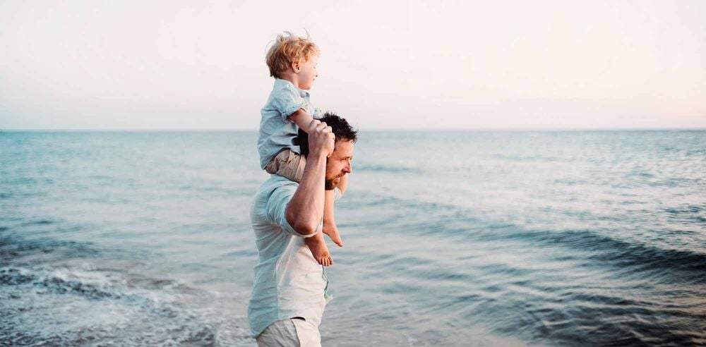 Papa portant son enfant sur les épaules face à la mer, accueillir un nouveau bébé en famille recomposée, trouver sa place de parent