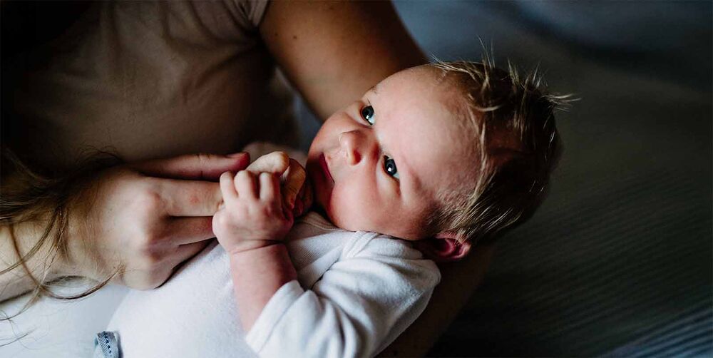 Nouveau-né aux yeux ouverts dans les bras de sa maman, avoir un bébé en famille recomposée, accueillir un nourrisson dans une fratrie existante
