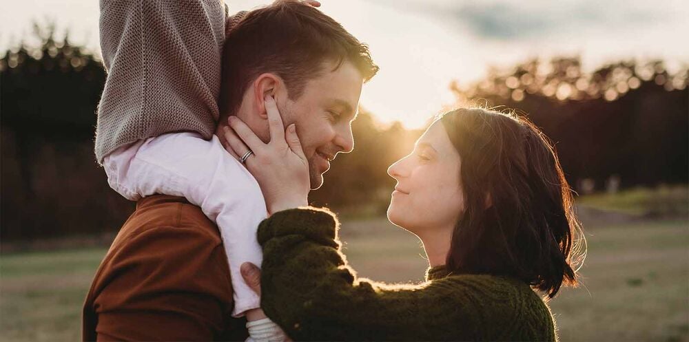 Couple complice au coucher du soleil avec enfant dans les bras, avoir un nouvel enfant en famille recomposée, l'importance du projet de couple