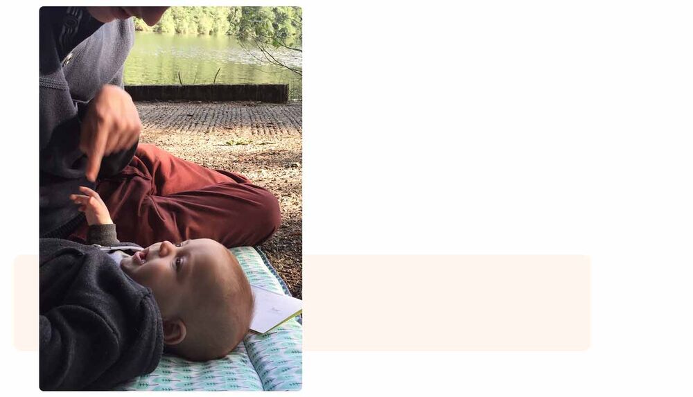Parent allongé avec bébé sur un tapis de jeu en plein air au bord de l'eau, camper avec son bébé, indispensables pour profiter du camping en toute sécurité