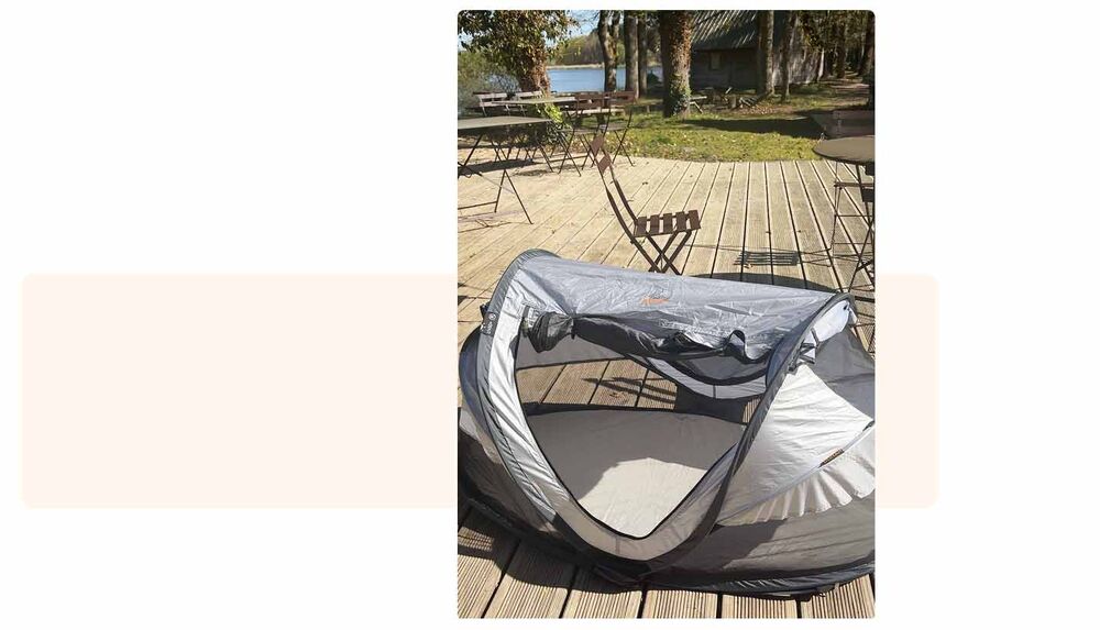Lit de voyage pop-up bébé installé sur une terrasse en bois face à un lac, checklist camping bébé, lit portable indispensable pour faire dormir bébé en extérieur