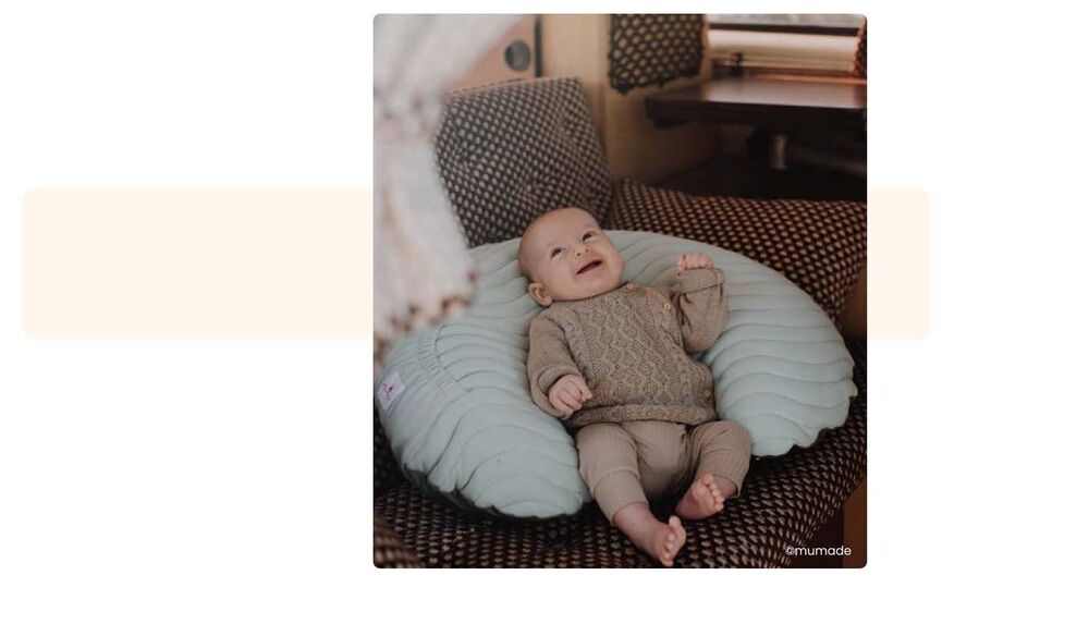 Bébé souriant installé dans un coussin d'allaitement dans un van aménagé, choisir son camping avec bébé, hébergement adapté et confortable pour les familles