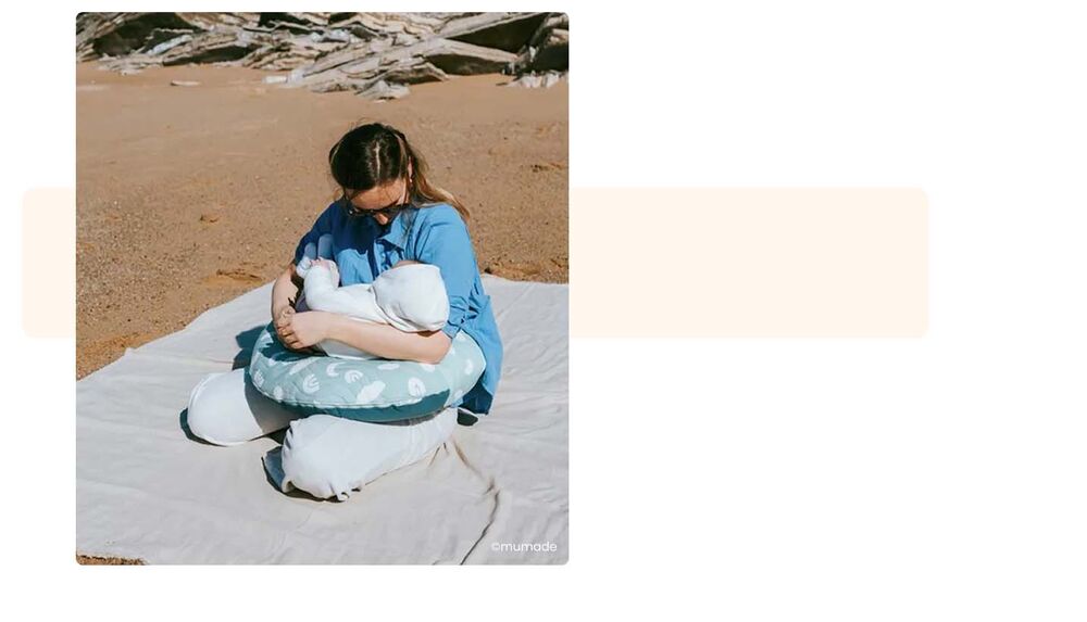 Maman allaitant son nouveau-né sur une plage avec coussin d'allaitement, conseils pour partir camper avec un bébé, allaitement et confort en plein air