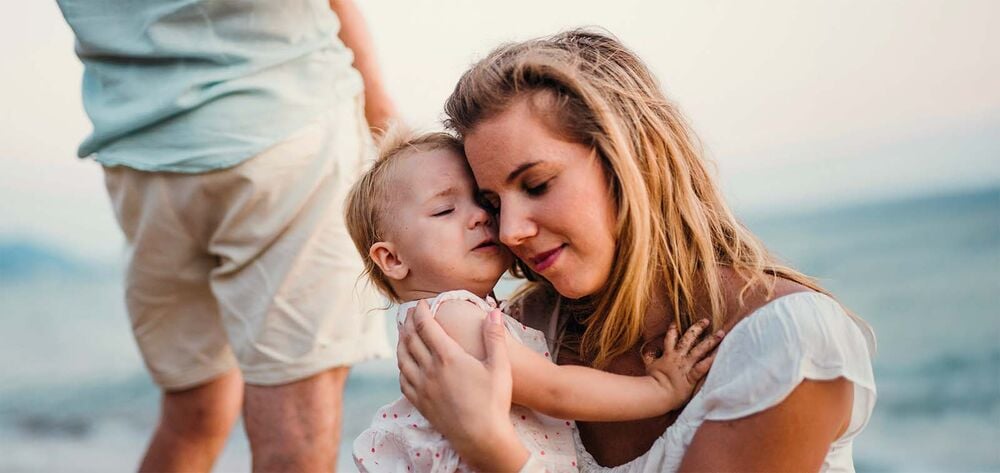 Maman serrant tendrement sa fille contre elle au bord de l'eau, construire une famille recomposée épanouie, créer des liens forts entre enfants