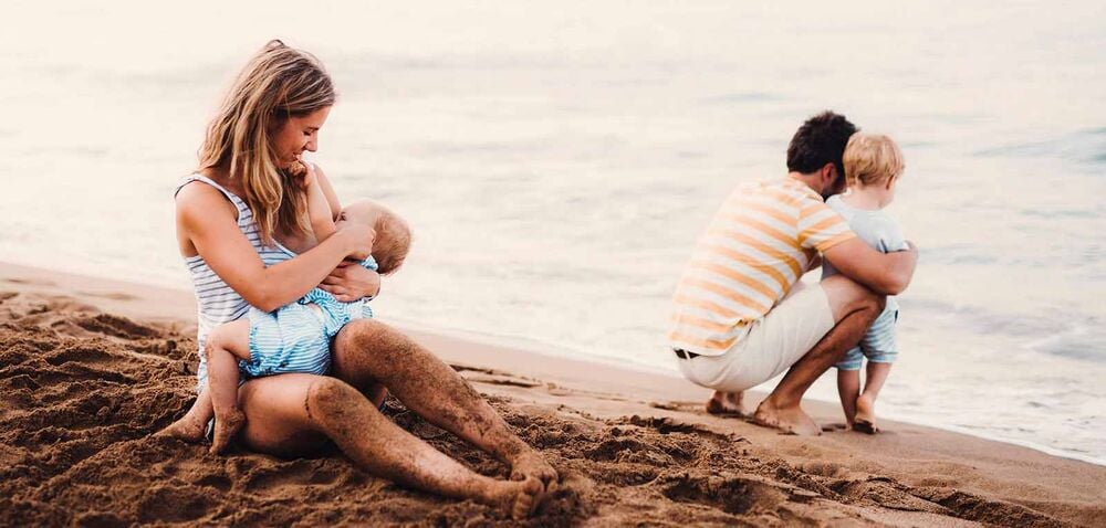 Parents et deux enfants sur la plage, maman allaitant et papa avec le grand, astuces pour gérer l'arrivée d'un bébé en famille recomposée avec enfants