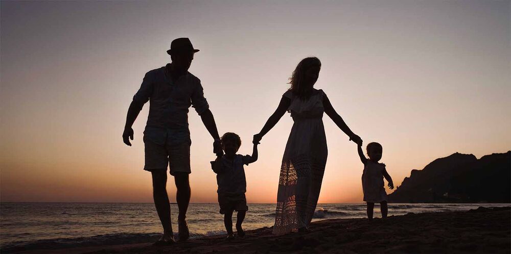 Silhouette d'une famille de quatre au coucher du soleil sur la plage, famille recomposée comment trouver sa place quand arrive un nouveau bébé