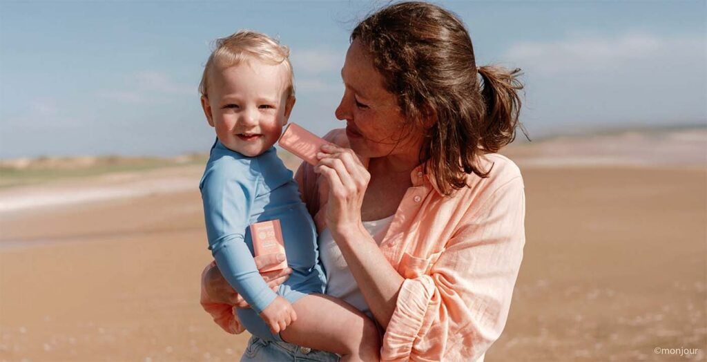 Maman appliquant de la crème solaire sur son enfant à la plage, meilleurs conseils protection solaire bébé en été