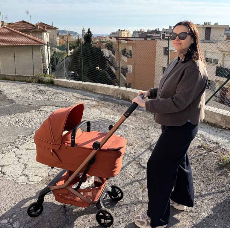 Maman poussant une poussette nacelle Maxi-Cosi terracotta en ville, partir en voyage avec une poussette nouveau-né pratique et légère