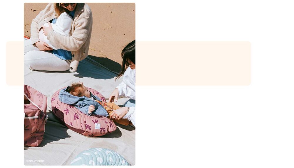 Maman allaitant et bébé installé sur un coussin d'allaitement sur la plage, produits soin et hygiène bébé camping, indispensables à glisser dans le sac