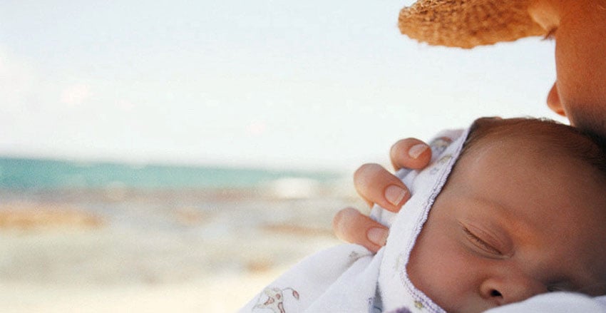 Nouveau-né endormi sur l'épaule de sa maman au bord de la mer, protéger bébé de la chaleur, éviter l'exposition directe au soleil dès la naissance
